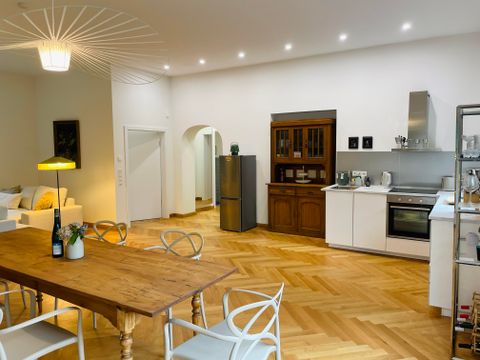 Eine moderne Küche mit Holzfußboden und einem großen Esstisch. Im Hintergrund steht eine Sitzecke und eine Kücheneinrichtung.