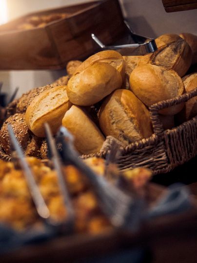 A basket of fresh rolls and various baked goods. The rolls are golden brown and attractively arranged.