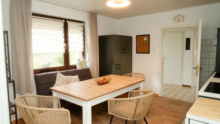 Une cuisine lumineuse avec un coin repas comprenant une table en bois et quatre chaises. Beaucoup de lumière entre par les fenêtres, créant une atmosphère accueillante.