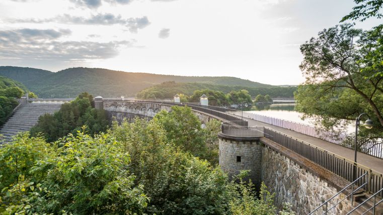 Blick auf die Urftstaumauer mit Wanderweg und umliegender Natur.
