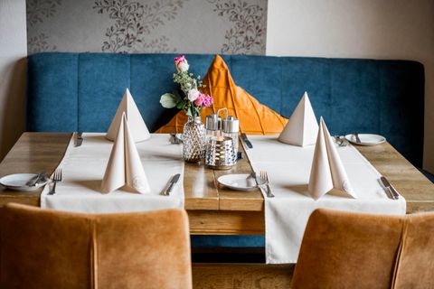 Ein gedeckter Tisch in einem stilvollen Restaurant. Die Dekoration umfasst elegante Servietten, Besteck und eine Blumenvase.