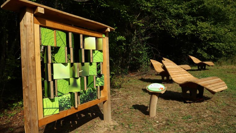 On voit une station où les enfants doivent résoudre une énigme d'image. À l'arrière-plan, il y a des bancs pour se reposer au soleil.
