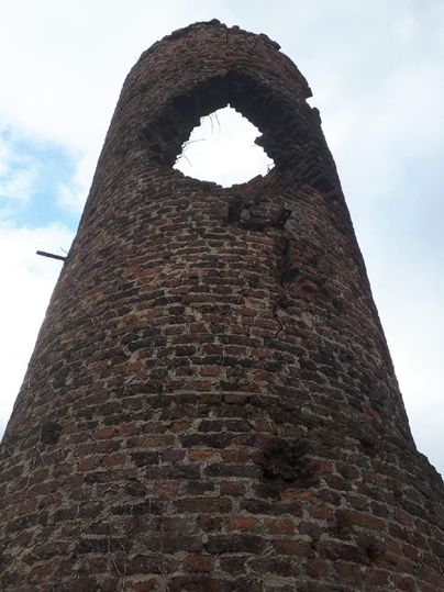 An old, crumbling tower made of red bricks with a large hole at the top. The sky is overcast and it feels bleak.