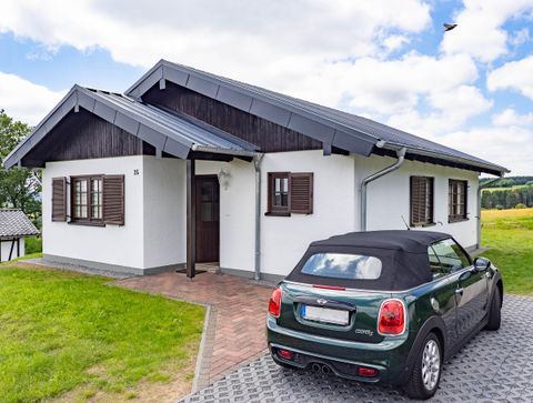 A modern house with a gray roof and white walls. In front of the house is a small black sports car.