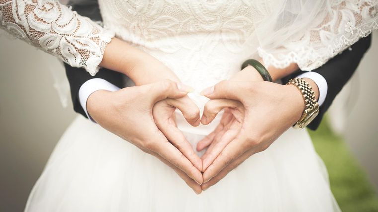 Deux mains forment un cœur, tandis qu'elles portent une robe de mariée. Cela symbolise l'amour et l'affection.