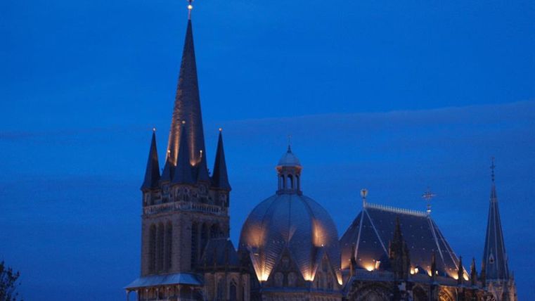 Une cathédrale impressionnante avec des tours hautes et un toit en dôme saisissant, illuminée au crépuscule. Le ciel est bleu foncé, donnant à la scène une atmosphère mystique.