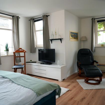 A bright bedroom with a bed, a television (HDMI connection and Blu-ray player), and a comfortable armchair. Various movies are available on-site.