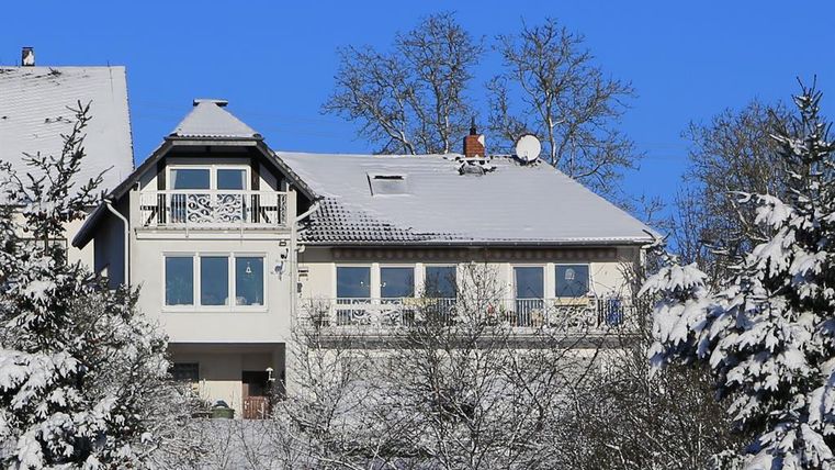Een modern huis in de sneeuw met een helder blauwe lucht. De omgeving is omringd door met sneeuw bedekte bomen.