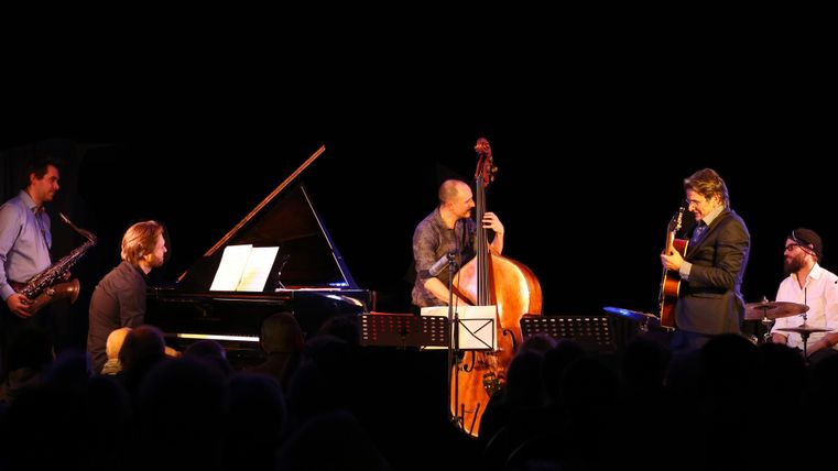 Eine Jazzband spielt live auf der Bühne. Die Musiker sind mit verschiedenen Instrumenten beschäftigt und die Atmosphäre ist lebhaft.
