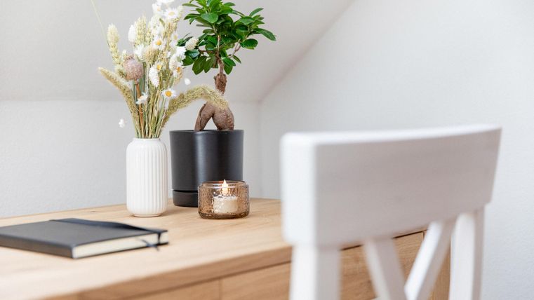 Ein schöner Schreibtisch mit einer Vase, einer Pflanze und einem Notizbuch. Der Raum wirkt hell und einladend.