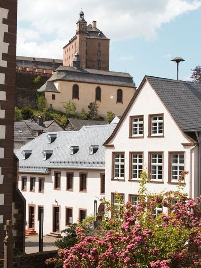 Kasteel Malberg op de achtergrond met moderne gebouwen en bloeiende struiken op de voorgrond.