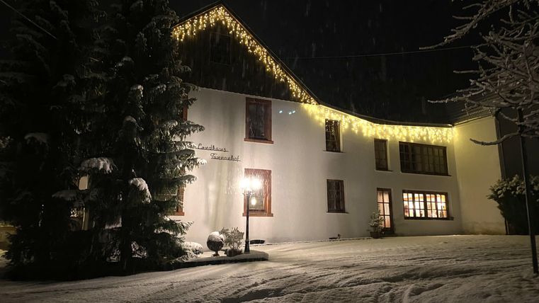Een mooi huis in de sneeuw, verlicht met lichtsnoeren. Het landschap is winterachtig en er heerst een rustige sfeer.