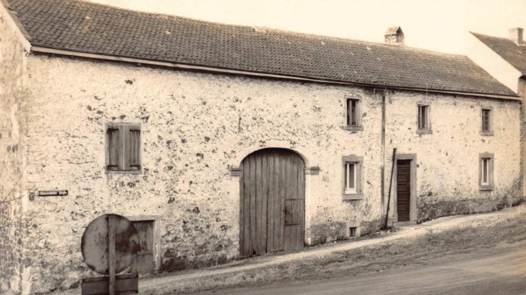 An old, stone building with a large wooden door and windows. The street in front is quiet and the sky is clear.