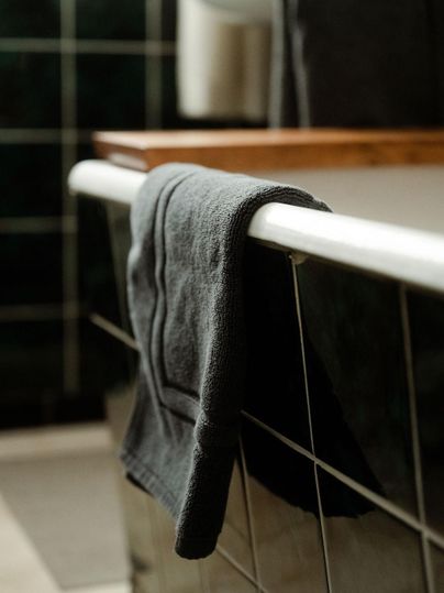 Une serviette noire est suspendue au bord d'une baignoire. En arrière-plan, des carreaux verts et une table en bois sont visibles.