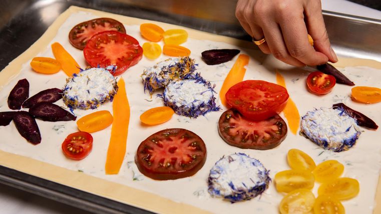 Een metalen plaat met verse groenten en kaas. Iemand decoreert de ingrediënten voorzichtig met verschillende groenten.