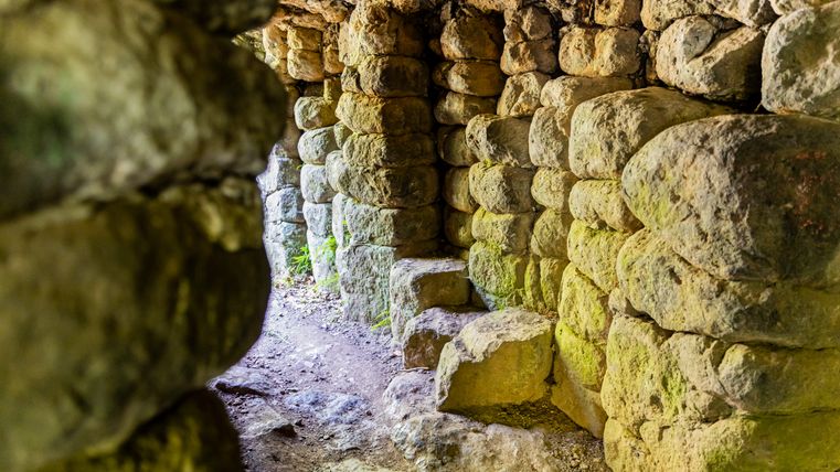 Een oude stenen tunnel met ruw uitgehouwen rotsen die naar de open lucht leidt.