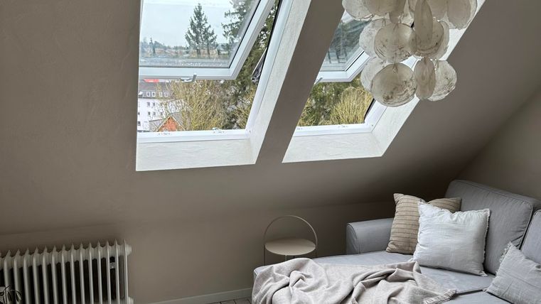 Een gezellige woonkamer met een moderne bank en een ronde tafel. De grote ramen laten veel daglicht binnen en bieden uitzicht op de buitenlucht.