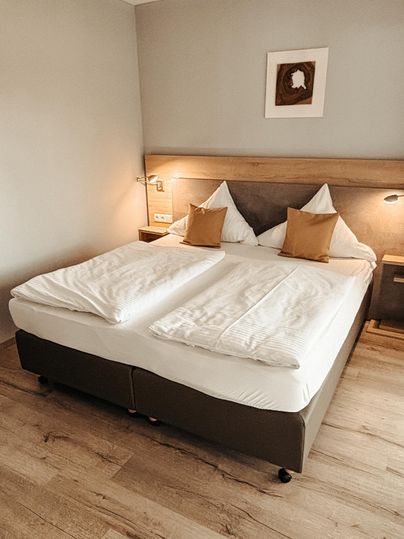 Une chambre moderne avec un grand lit double. Les murs sont clairs et neutres, et il y a une lumière chaude qui crée une atmosphère cosy.