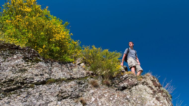 A hiker stands on a rocky outcrop under a blue sky.