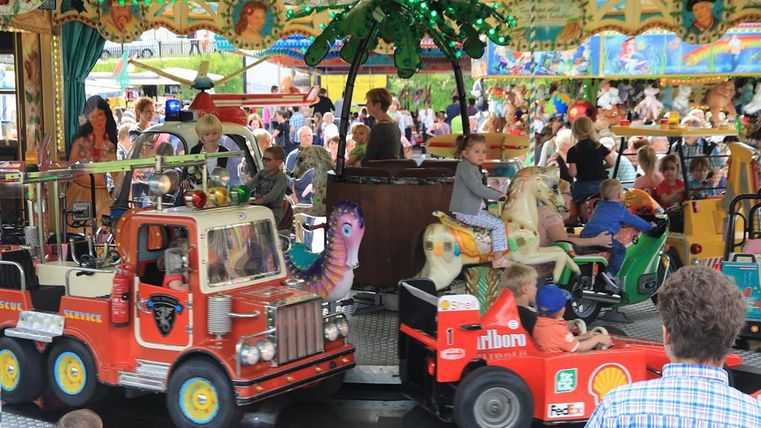 Buntes Kinderkarussell mit unterschiedlichen Fahrzeugen, in denen glückliche Kinder sitzen.
