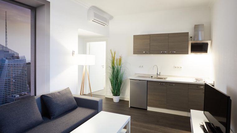 Ein modernes Wohnzimmer mit einer Küchenzeile und einer Couch. Der Raum ist hell und freundlich gestaltet.