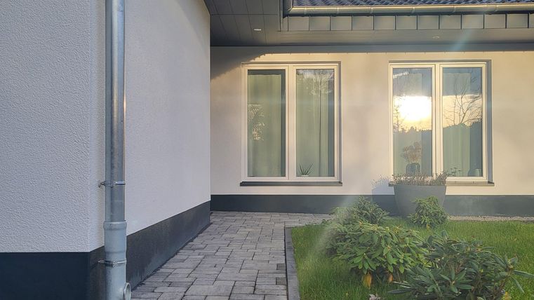 Een moderne entree met een geplaveide stenen weg. Te zien zijn ramen en een verzorgde grasmat op de voorgrond.