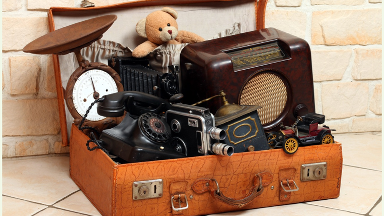 Ein vintage Koffer voller alter Gegenstände, darunter eine Kamera, eine Uhr, ein Plattenspieler und ein teddy. Der Koffer vermittelt ein Gefühl von Nostalgie und Geschichte.