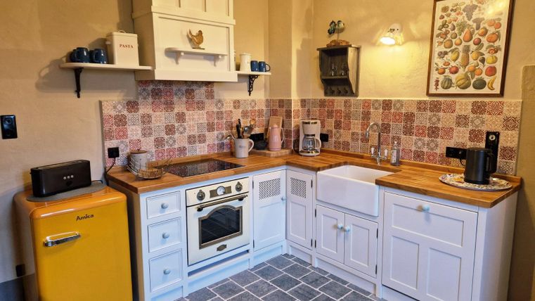 A modern kitchen with a yellow refrigerator and a white sink. The walls are decorated with colorful tiles, and there are wooden surfaces as well as a cozy atmosphere.