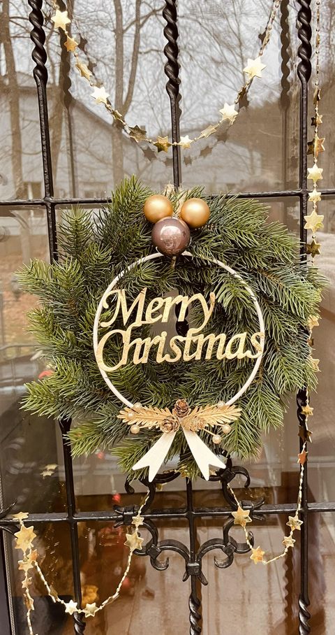 A Christmas wreath hangs on a door. It is adorned with a golden "Merry Christmas" message and decorative baubles.