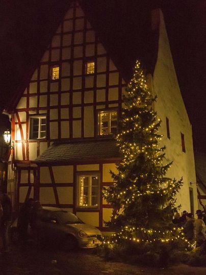 Een traditioneel vakwerkhuis met verlichte ramen in de nacht. Naast het huis staat een versierde kerstboom.