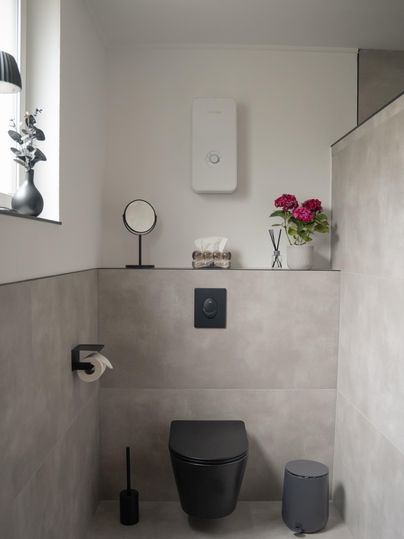 Een moderne badkamer met grijze muren en een stijlvolle zwarte wc. Op de plank staan decoraties en bloemen in een vaas.