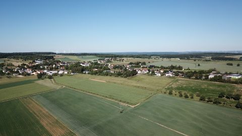 Luftbild von Idenheim mit Feldern und Windrädern im Hintergrund.