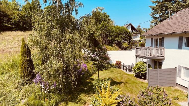 Een mooie tuin met verschillende planten en een kleine vijver. Op de achtergrond staat een huis met een balkon.