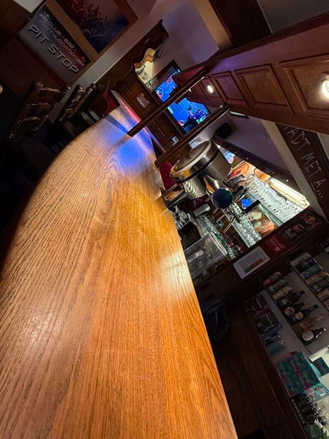 Een gezellige barruimte met een lange houten toog. Op de achtergrond zijn dranken en een televisie te zien.