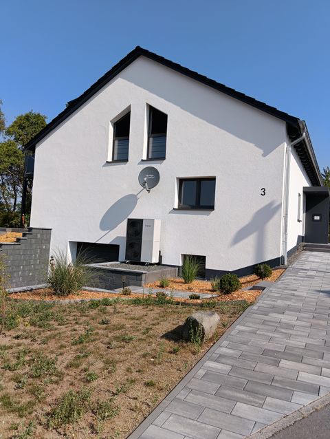 Een modern, wit huis met een aantrekkelijk ontwerp. De voortuin is verzorgd en met stenen en planten aangelegd.