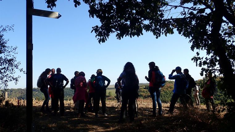 Eine Gruppe von Wanderern steht vor einem Aussichtspunkt. Im Hintergrund ist ein klarer Himmel und die Landschaft zu sehen.