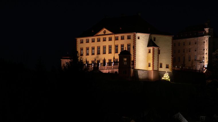 Un château imposant la nuit, éclairé par une lumière chaude.
Entouré d'arbres sombres et du ciel nocturne.