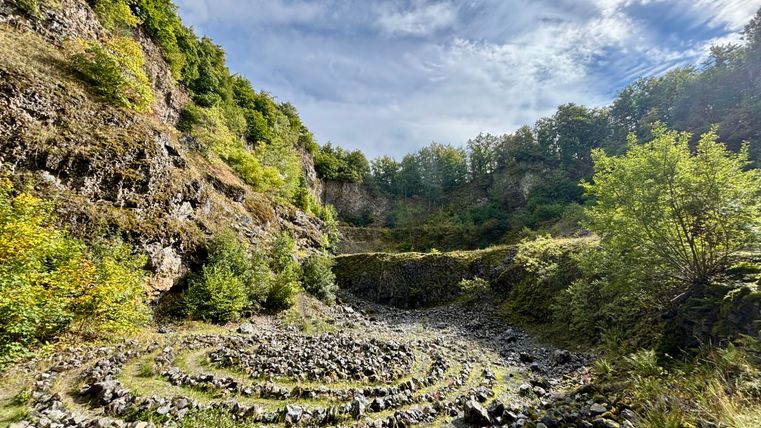 Stone spiral in the Arensberg volcano with wooded rock faces and blue sky.
