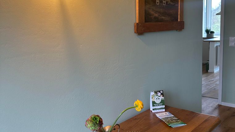 Ein einladender Flur mit einem Holztisch, dekoriert mit einer kleinen Blume in einer Vase. An der Wand hängt ein Bild und es gibt eine warm leuchtende Lampe.