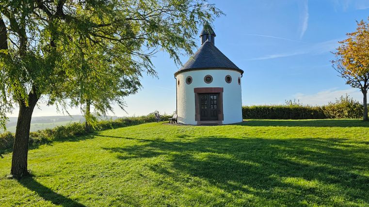 Round chapel on a meadow with trees, blue sky.