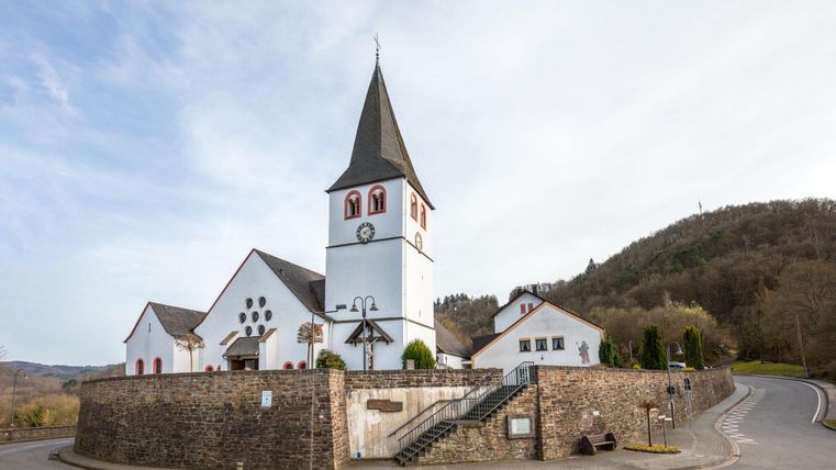 A beautiful church with a distinctive bell tower stands at a street corner. In the background, gentle hills can be seen.