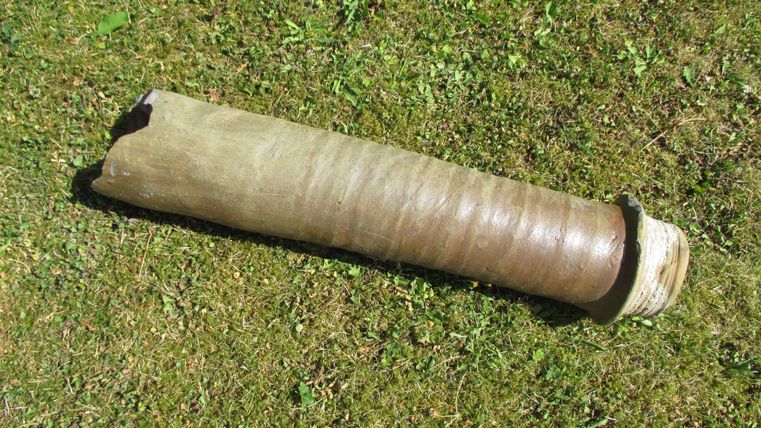 Un objet long et cylindrique est posé sur de l'herbe verte. Il a une surface lisse et une extrémité arrondie.