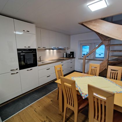 Moderne keuken met witte kasten en een houten trap. Een grote eettafel met stoelen nodigt uit om te blijven hangen.