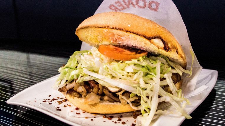 Symbolbild: Auf einem weißem Teller liegt ein Döner. In dem geöffneten Flydenbrot liegen geschichtet. kleingeschnittenes fleisch, Salat und Tomaten.