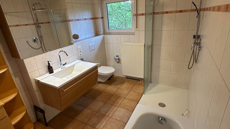 Ein modernes Badezimmer mit einer Badewanne und einer Dusche. Helle Fliesen und Holzdecke sorgen für eine freundliche Atmosphäre.