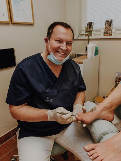 De heer Spengler voert een voetbehandeling uit in zijn praktijk. De patiënt wordt vriendelijk begeleid, terwijl de behandelaar glimlacht.