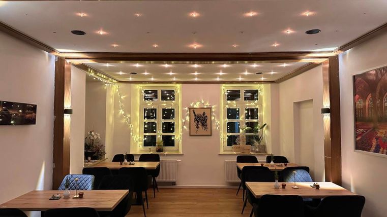 An elegant restaurant with modern design and atmospheric lighting. The tables are neatly set, and large windows provide a view outside.