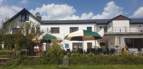Een gezellig café met parasols en een uitnodigend terras. De omgeving is groen en er is een heldere blauwe lucht.