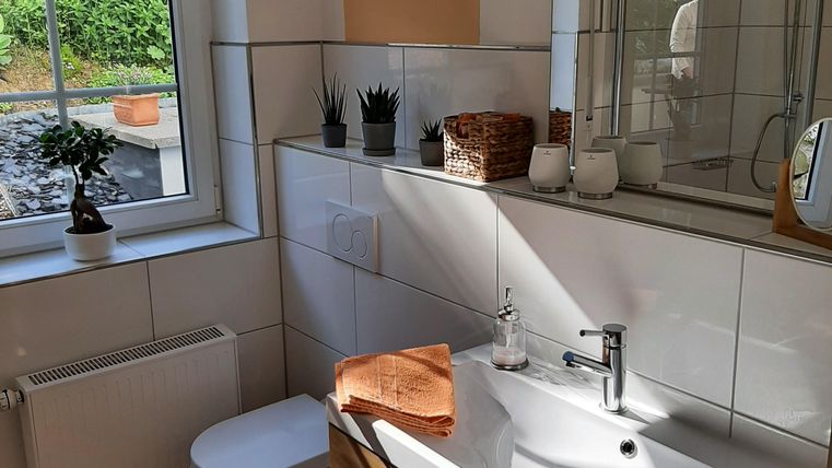 Ein modernes Badezimmer mit hellem Fliesenboden und Holzschränken. Natürliches Licht fällt durch das Fenster und sorgt für eine freundliche Atmosphäre.