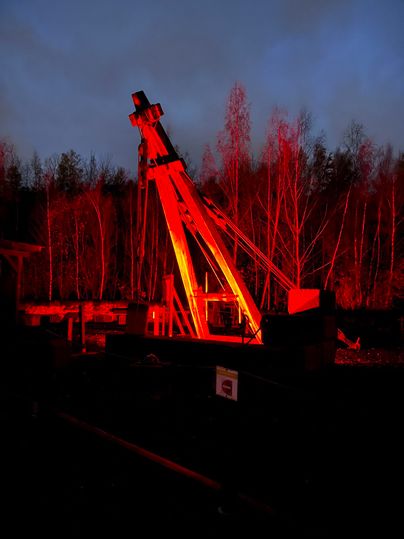 Eine rote Beleuchtung erhellt eine große technische Struktur in einer Waldlandschaft. Die umgebenden Bäume sind teilweise im Dunkeln verborgen.
